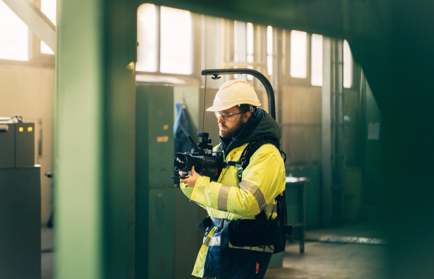 Daniel filmt mit Helm und Warnjacke in einer Industriehalle